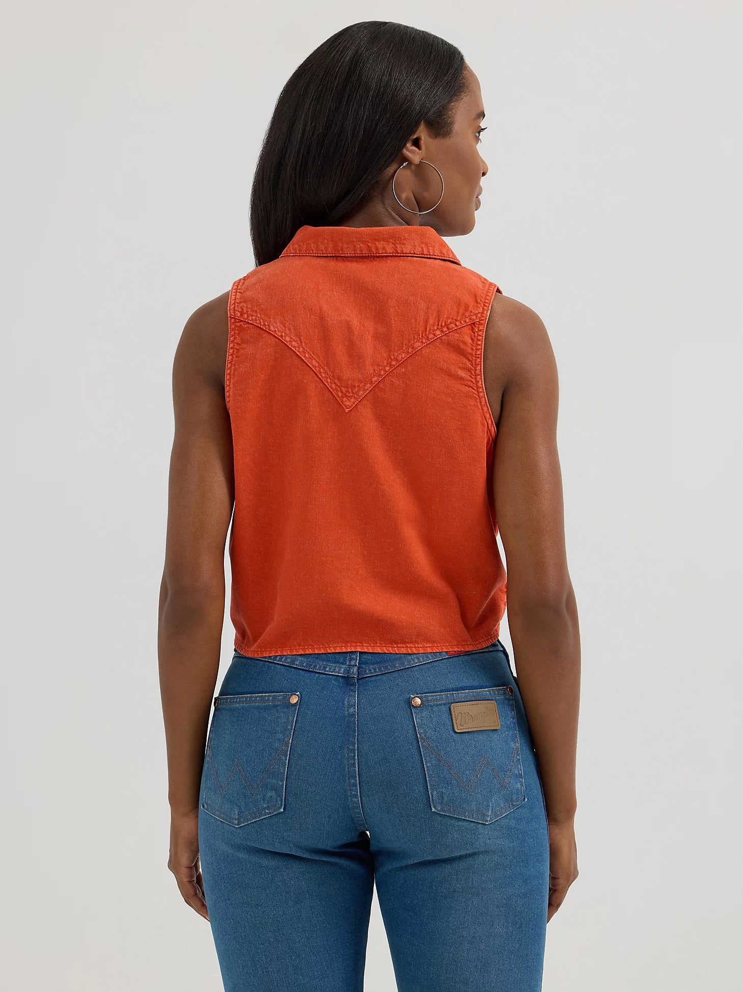 Woman wearing an orange sleeveless denim vest and blue jeans on a white background